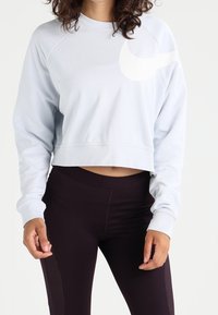 Ljusblå kort sweatshirt med raglanärmar och en stor vit logotyp på bröstet, ihop med svarta leggings med texturerade detaljer.