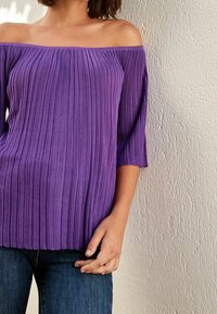 Top viola, scollo a barca con texture a righe verticali, maniche 3/4 e vestibilità rilassata, abbinato a jeans blu.