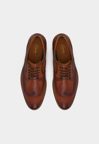 Ζευγάρι γυαλιστερά καφέ δερμάτινα παπούτσια μπρόγκες με μαύρα κορδόνια, απόψη πάνω σε απλό λευκό φόντο.