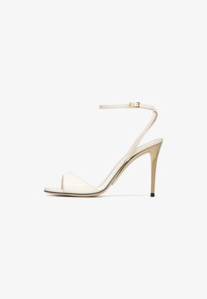 Beige high-heeled sandal with slim ankle strap and gold-tone buckle, open toe, and metallic stiletto heel.