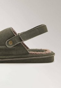 Green suede sandal with a strap and brass snap detail. Soft beige lining, flat sole, and rounded shape for comfort.