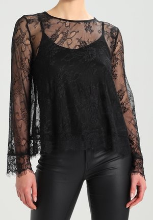 Black floral lace long-sleeve top over a black camisole, paired with black fitted leather pants, worn by a standing person.