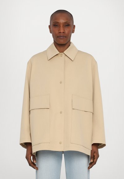 Giacca oversize beige realizzata in materiale morbido, con colletto classico, grandi tasche frontali e chiusura a bottoni. Tessuto liscio.