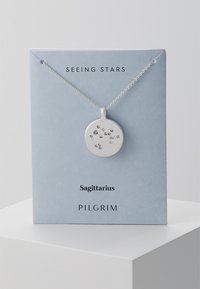 Silberner Anhänger mit kreisförmiger Form, verziert mit verstreuten Edelsteinen, die das Sternbild Schütze darstellen, präsentiert auf einer hellblauen Karte.