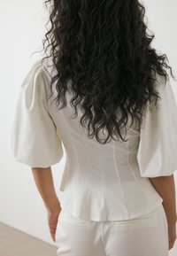 Witte gestructureerde blouse met pofmouwen, getailleerde lijfje en uitlopende zoom. Glad textiel met verticale naden, gestyled met bijpassende broek.