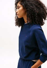 Sudadera azul marino con cuello redondo y mangas largas, con un pequeño logo en el pecho. Hecha de una tela suave y texturizada.