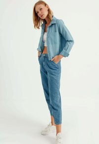 Lichtblauw overhemd met kraag, borstzak en opgerolde mouwen, gecombineerd met aansluitende lichtdenim jeans en witte sneakers.