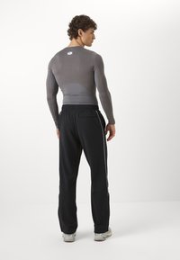 Grå langermet topp med et tettsittende design og en kontrasterende bakpanel, paret med svarte løstsittende bukser med hvite sidestriper.