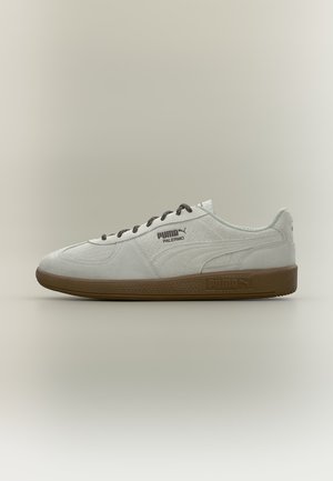 Λευκό αθλητικό παπούτσι Puma Palermo με μαύρα κορδόνια και καφέ σόλα, πλάγια όψη που δείχνει το λογότυπο Puma και ανάγλυφο επάνω μέρος από σουέντ.