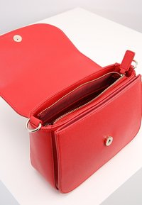 Röd läderhandväska med en slät textur, med en klaffstängning, guldfärgad hårdvara och dragkedjefickor inuti.