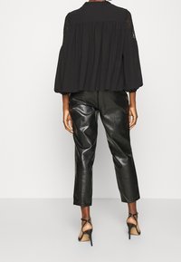 Blouse noire avec accents en dentelle, corsage froncé et manches bouffantes, associée à un pantalon noir en similicuir taille haute et des talons noirs à brides.