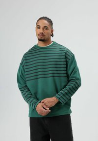 Groene sweatshirts met horizontale zwarte strepen over de bovenkant van de borst en mouwen. Gemaakt van zachte stof met een comfortabele pasvorm.