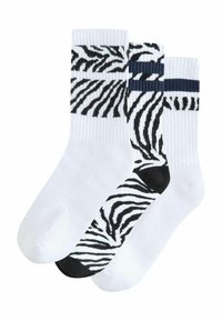 Tri par bijelih pamučnih čarapa: dvije sa bijelim i crnim zebrastim prugama, jedna potpuno bijela s tamnoplavim detaljima na vrhu.