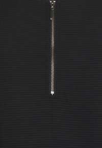 Haut zippé noir en tissu texturé avec un motif en côtes et un détail en métal argenté pour la fermeture.