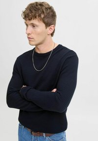 Pull noir à manches longues côtelé avec un col rond, présentant une finition texturée et une coupe régulière, associé à un jean en denim bleu clair.