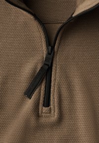 Hnědý svetr s texturovanou tkaninou, s předním dílem na polovinu zipu a černým zipem. Na táhle zipu je vyryto "HLEDEJ DOBRODRUŽSTVÍ".