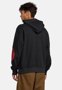 Schwarzer Hoodie mit lässiger Passform, ausgestattet mit roten Grafikprints auf den Ärmeln, weichem Material und einer verstellbaren Kapuze mit Kordelzug.