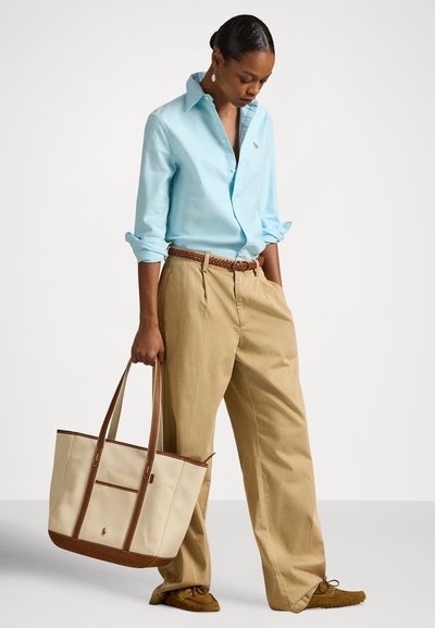 Gaiši zila pogām aizpogājamā krekls, bēša plaša piegriezuma bikses, brūns austs josta un gaiši brūna soma ar ādas akcentiem un logotipu.