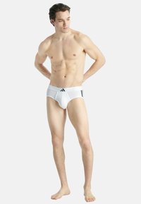 Bañador atlético blanco con una textura suave. Presenta una amplia cinturilla elástica con tres rayas negras. Diseñado para la comodidad y el soporte.