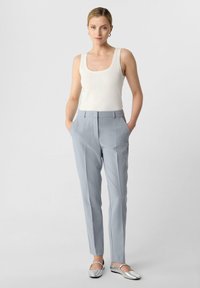 Lichtgrijze op maat gemaakte broeken met scherpe plooien, gecombineerd met een aansluitend wit tanktop. De outfit heeft zilveren ballerina's en geen zichtbare patronen.