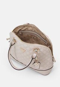Quilted beige handbag with a zip closure, gold hardware, dual handles, and interior zip pocket; features a logo charm and patterned lining.