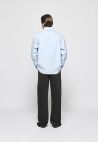 Lichtblauw longsleeve shirt met een button-down kraag, gecombineerd met donkergrijze rechte broek. Gladde stof, ontspannen pasvorm.