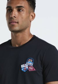 Zwarte katoenen t-shirt met een ronde halslijn en drie kleurrijke geborduurde patches met tekst en ontwerpen op het linkerborstgebied.