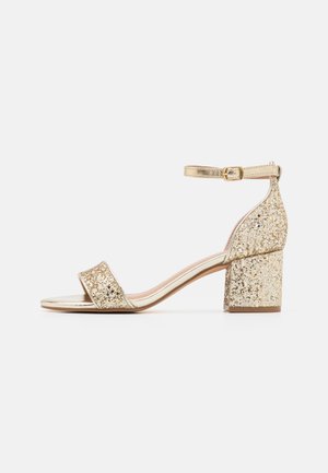Gul blokhælede sandal med glitrende overdel og metallisk rem. Har en justerbar ankelspænde og åbent tådesign. Glat tekstur.