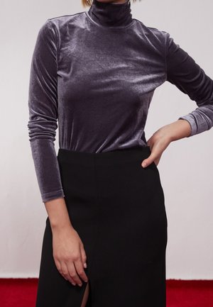 Un haut à manches longues et col montant en velours violet doux et discret, associé à une jupe noire taille haute avec une fente sur le côté.