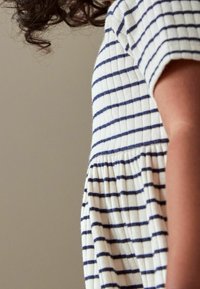 Pasiasta sukienka w białym i granatowym kolorze, z prążkowaną fakturą, krótkimi rękawami i marszczoną spódnicą. Skupienie na widoku z boku sukienki.