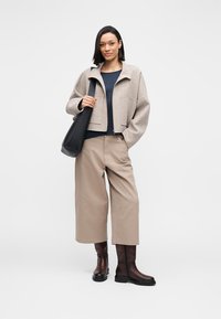 Beżowa krótka kurtka z wełny, granatowa bluzka, beżowe spodnie o szerokich nogawkach oraz brązowe kozaki za kolano. Czarna torba na ramię o gładkiej fakturze.