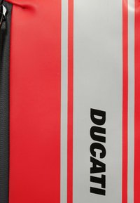 Zaino rosso e grigio con il prominente logo nero "DUCATI", caratterizzato da una texture liscia e da due strisce verticali per un accento di design.