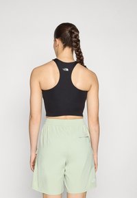 Must have musta crop-top, millel on sõidurihma disain, koos heleda rohelise lühikese püksiga, millel on küljetaskud. Minimalistlik bränding peal.