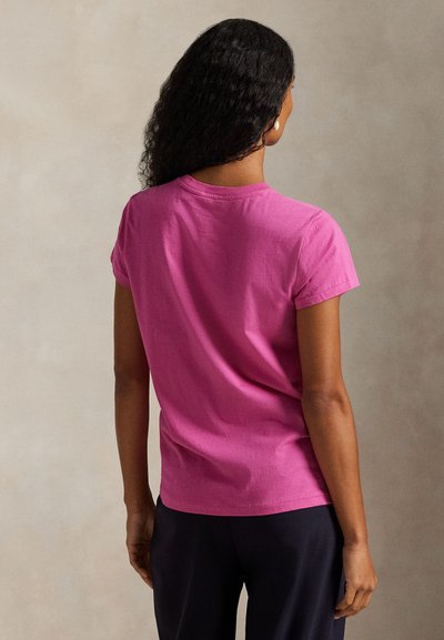 Εφαρμοστή κοντομάνικη μπλούζα σε έντονο ροζ βαμβάκι. Απλό σχέδιο με στρογγυλή λαιμόκοψη και λεία υφή, παρουσιάζεται από πίσω.