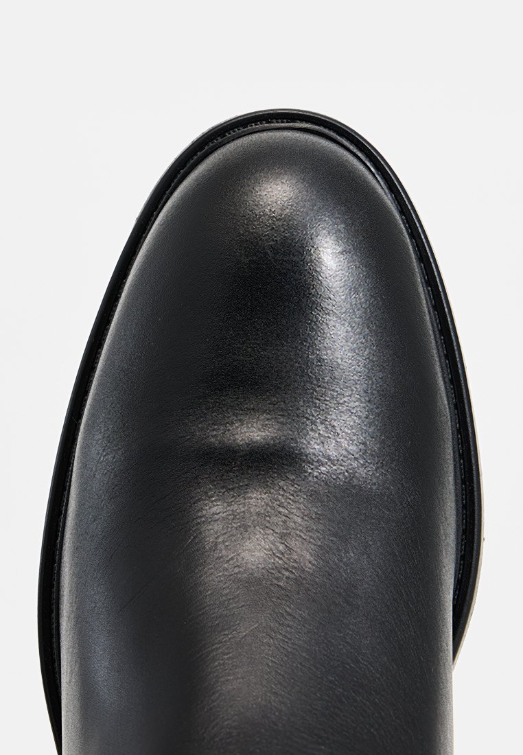 Botín de cuero negro con punta redondeada, textura suave y costuras mínimas. Diseño elegante con un acabado brillante y un sutil brillo.