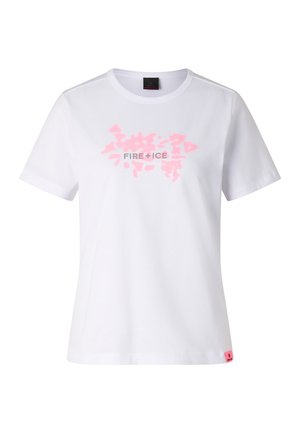 Femme blonde portant un t-shirt graphique blanc avec l'inscription « FIRE + ICE », un pantalon ample gris clair et des sneakers blanches, debout devant un fond uni.