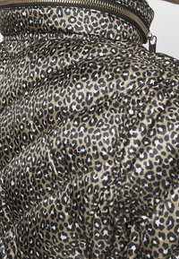 Doudoune avec un motif léopard en beige et noir. Fabriquée en matériau matelassé brillant avec des coutures visibles et une fermeture éclair.