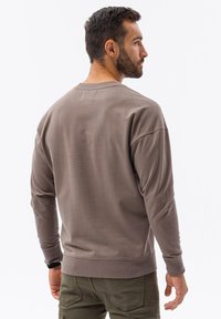 Hnědá mikina s dlouhým rukávem a kulatým výstřihem, s žebrovanými manžetami a lemem, a hladkou texturou, nošena modelem ze zezadu.