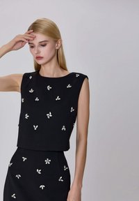 Robe noire à silhouette ajustée, col rond, ornée de motifs floraux en tons argentés sur tout le tissu.