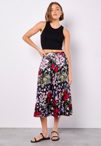 Blumige Midirock mit schwarzem Grund, der bunte Muster aus pinken, roten und lila Blumen zeigt; elastischer Taillenbund; kombiniert mit einem schwarzen Cropped-Top.