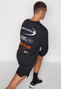Musta pikade varrukatega särk, mille seljal on valged ja oranžid graafikud, sisaldades logosid, telefoninumbrit ja sportlikku disaini.