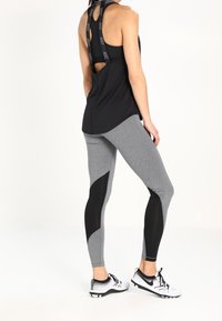 Czarny sportowy top na ramiączkach z podwójnymi paskami, w połączeniu z dopasowanymi szarymi legginsami z czarnymi akcentami w geometryczne wzory. Białe buty sportowe dopełniają wygląd.