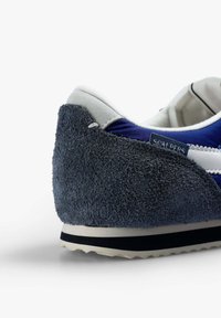 Zapatilla con parte superior de tela azul marino, capucha de talón de ante gris, franjas blancas y suela de goma texturizada con una línea de acento negra.