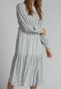 Lekka, midi sukienka w kremowo-niebieski kwiatowy wzór. Posiada marszczony gorset, długie bufiaste rękawy oraz falbankowy, warstwowy dół.