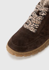 Baskets en suède marron avec des lacets à imprimé léopard et une épaisse semelle en caoutchouc beige sur fond blanc.