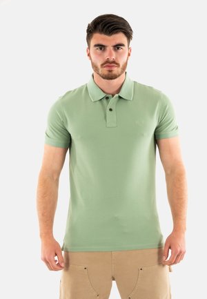 Polo in verde chiaro, con colletto e due bottoni. Maniche corte e un logo discreto sul petto. Tessuto morbido.
