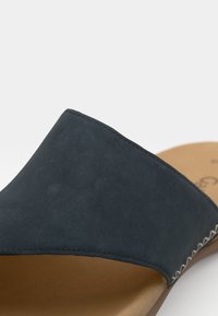 Mörkblå mocka slide-sandal med en bred rem, sömnadsdetaljer och en ljusbrun innersula, som har en slät yta och enkel design.