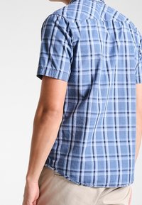 Camicia a maniche corte a quadri blu con colletto button-down. Presenta strisce blu chiare e scure, realizzata in un tessuto leggero con orlo curvo.