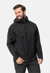 Schwarze wasserdichte Jacke mit Kapuze, ausgestattet mit zwei verschließbaren Brusttaschen, verstellbaren Bündchen und einer glatten Textur. Logo auf der Vorderseite angebracht.