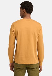Long-sleeve shirt in mustard yellow cotton, featuring a crew neck, set-in sleeves, straight hem, and a small logo tag at the bottom seam.